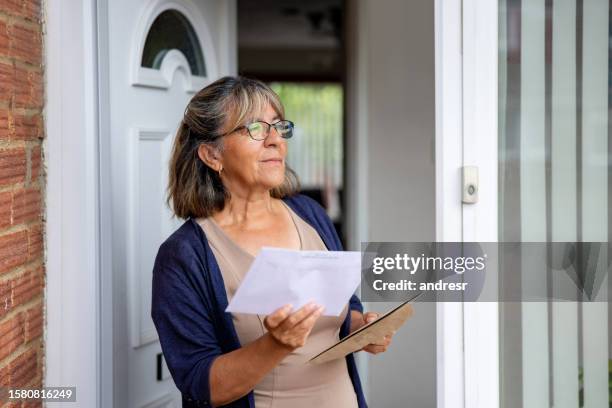 senior woman checking her mail at the front door of her house - elderly receiving paperwork stock pictures, royalty-free photos & images