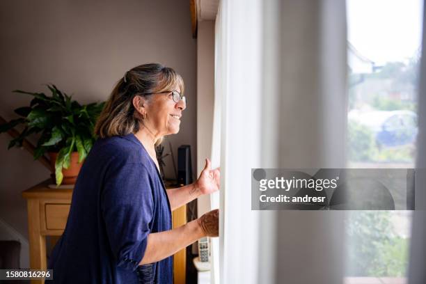 nosy senior woman at home looking at her neighbors through the window - apartamento municipal imagens e fotografias de stock