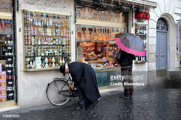 Cyclist chains his bicycle as a pedestrain looks at the window display of a delicatessen near Campo dei Fiori market in Rome, Italy, on Monday, Dec....