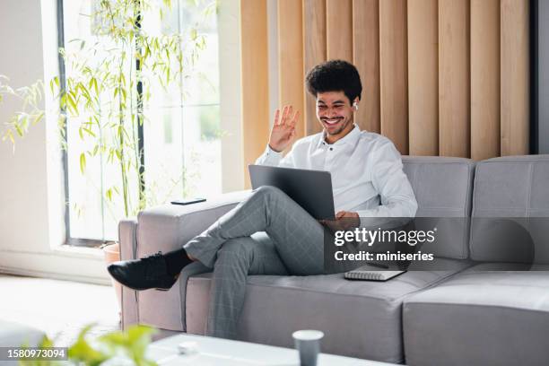 young smiling businessman sitting on a sofa and answering a video call - formal dress code stockfoto's en -beelden