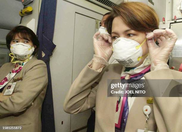 Philippine Airlines stewardesses on a flight bound for Singapore dons masks and gloves 28 April 2003 shortly before takeoff at Manila airport.The...