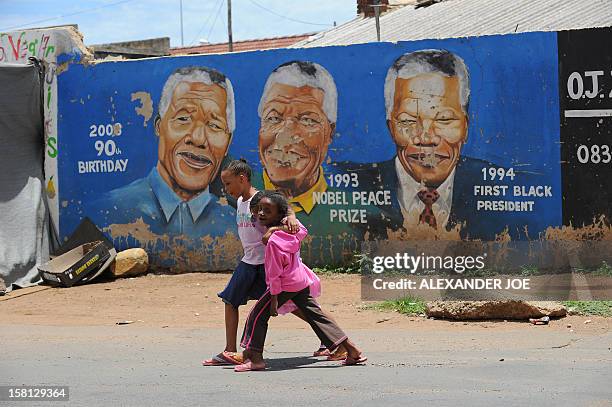 Soweto's residents walk past portraits of former South Africa's president Nelson Mandela painted on a wall, on December 10, 2012 in Soweto. Mandela...