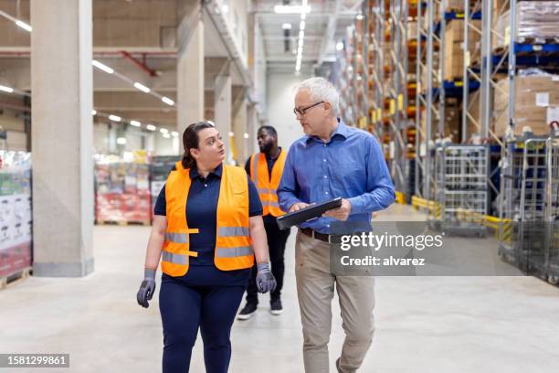 mature manager using digital tablet and discussing stock with female worker in warehouse - warehouse worker stock pictures, royalty-free photos & images