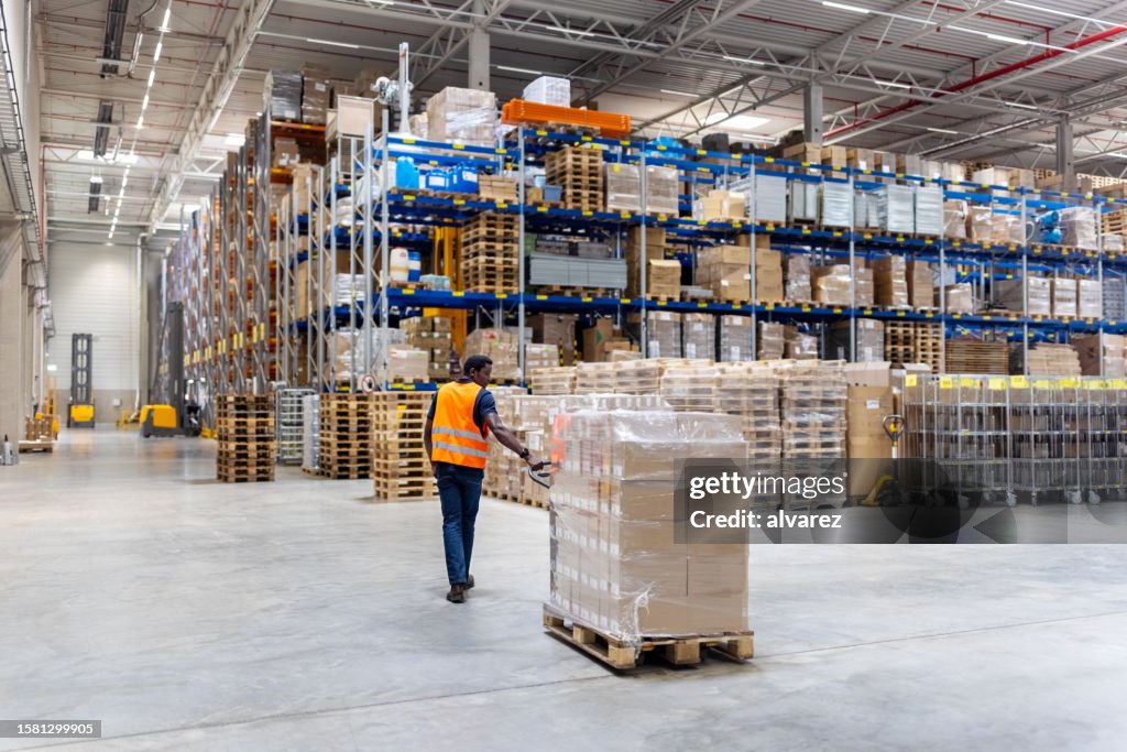 Young warehouse worker pulling pallet jack with boxes