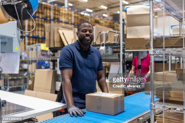 worker working in large distribution warehouse standing by conveyor belt - boxes conveyor belt stockfoto's en -beelden