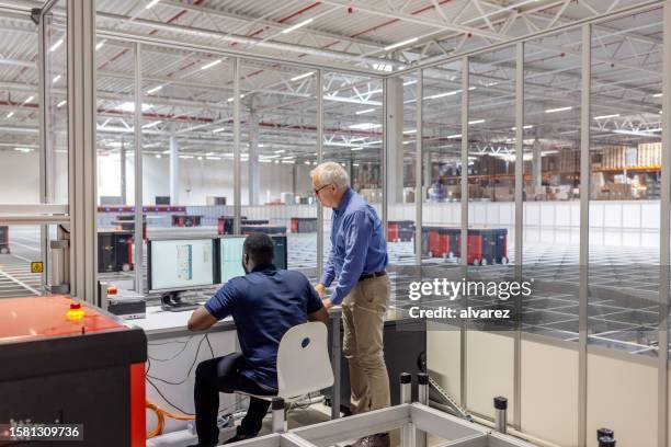 manager with a male worker working on computer in agv control room at warehouse - automated guided vehicles stockfoto's en -beelden