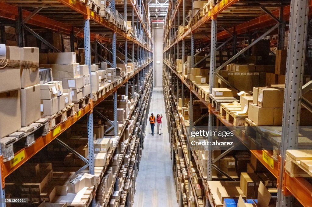 Blick aus der Vogelperspektive auf einen Lagerleiter, der mit Vorarbeitern den Bestand in den Regalen überprüft