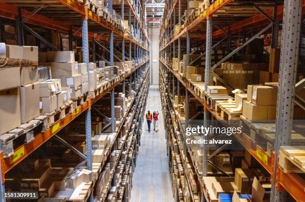 high angle view of a warehouse manager walking with foremen checking stock on racks - logistics warehouse stockfoto's en -beelden