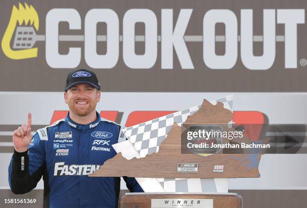 Chris Buescher, driver of the Fastenal Ford, celebrates with the checkered in victory lane after winning the NASCAR Cup Series Cook Out 400 at...