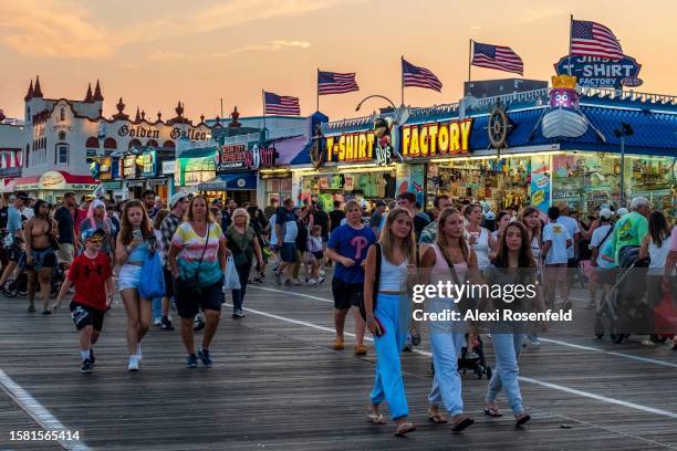 Large crowds of people walk along the Ocean City boardwalk near American flags flying during sunset on July 23, 2023 in Ocean City, New Jersey....