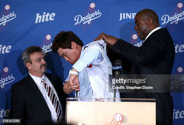 Dodger owner Ervin Magic Johnson and general manager Ned Colletti help Hyun-Jin Ryu put on his jersey at a press conference introducing him following...