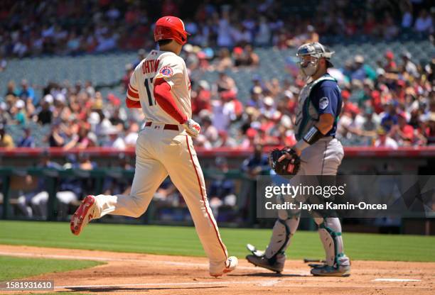 Cal Raleigh of the Seattle Mariners looks on as Shohei Ohtani of the Los Angeles Angels crosses the plate for a run in the first inning at Angel...