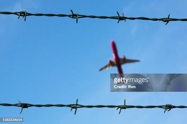 barbed wire with passenger aircraft in the sky - barbed wire stock pictures, royalty-free photos & images