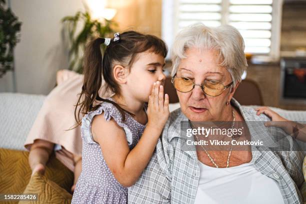 little girl whispering something to her grandmother at home - fluisteren stockfoto's en -beelden