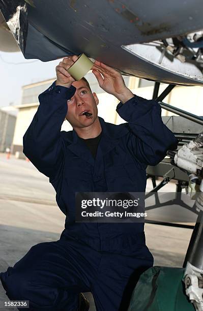 Senior Airman Ryan Fletcher, a crew chief for the 31st Aircraft Maintenance Squadron, applies masking tape to a F-16 panel opening to prevent water...