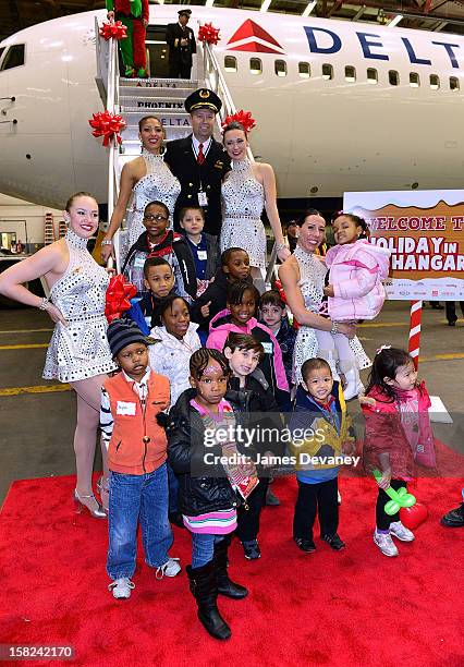 Delta pilot and the Radio City Rockettes pose with children at the 3rd Annual Garden of Dreams Foundation & Delta Air Lines' 'Holiday in the Hangar'...