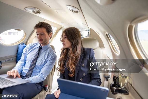 junges geschäftspaar, das in einem privatjet-flugzeug an einem digitalen tablet arbeitet - finanzen und wirtschaft stock-fotos und bilder