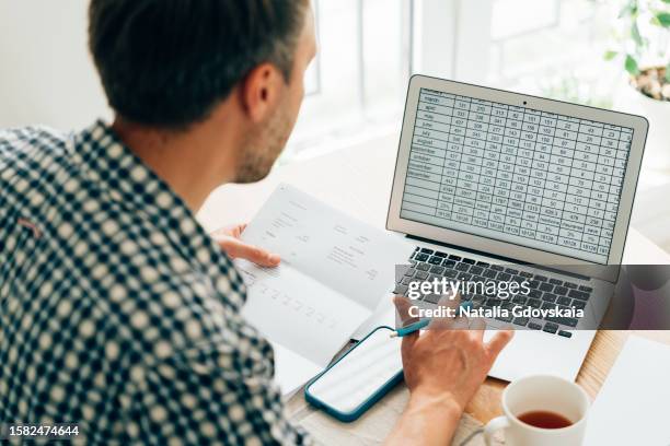 man using calculator, analyzing financial data. focused on work and working on budget or expense report. man sitting at table in well-lit office. - spreadsheet stockfoto's en -beelden