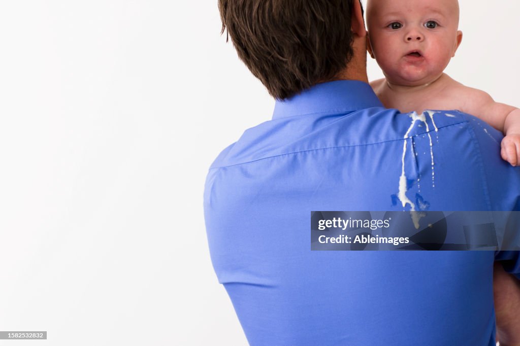 Back view of a man holding a baby with vomit on his back and shoulder