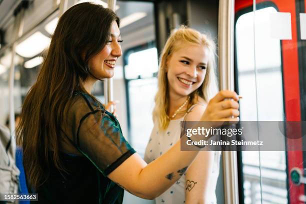 two young woman are standing in a train and smiling while riding through the city - zug stock pictures, royalty-free photos & images