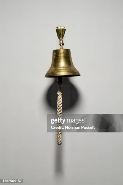 brass bell with rope pull hanging on wall - campana fotografías e imágenes de stock