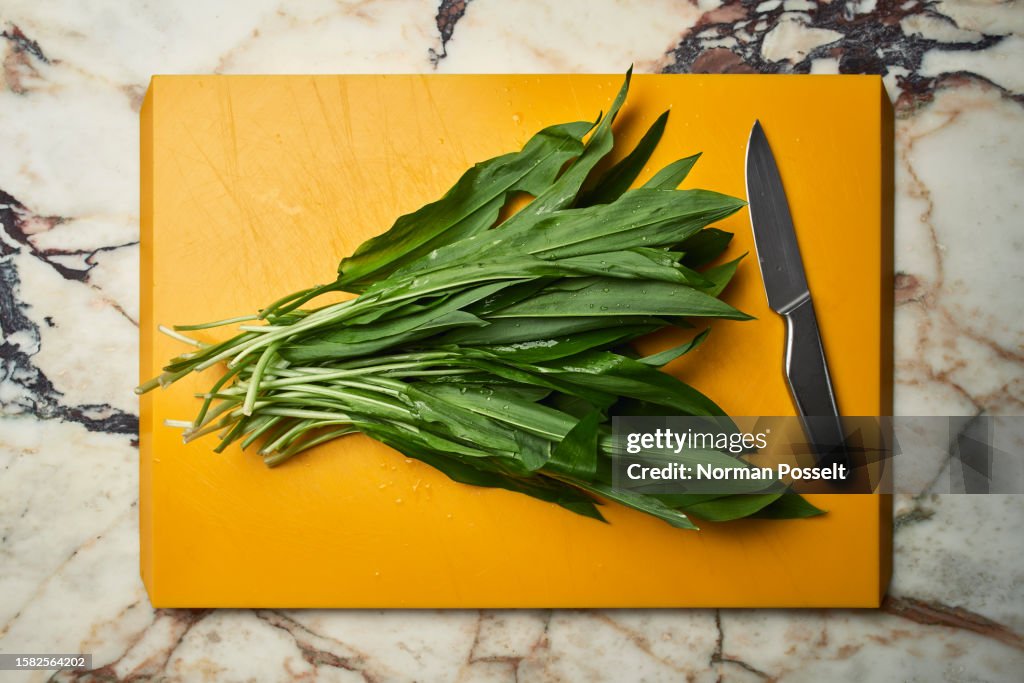 Green wild garlic leaves on cutting board next to knife
