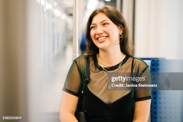 portrait of a young woman sitting in a train and smiling - gold chain necklace stock pictures, royalty-free photos & images