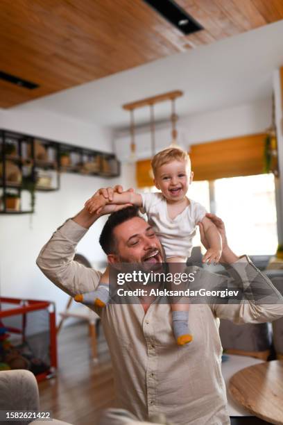 smiling baby boy enjoying ride on father's shoulders at home - funny baby photo stock pictures, royalty-free photos & images