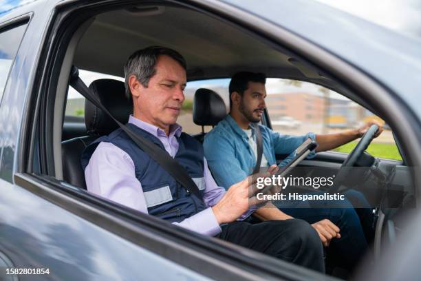 driving instructor using a tablet while grading a man's driving test - rijbewijs stockfoto's en -beelden
