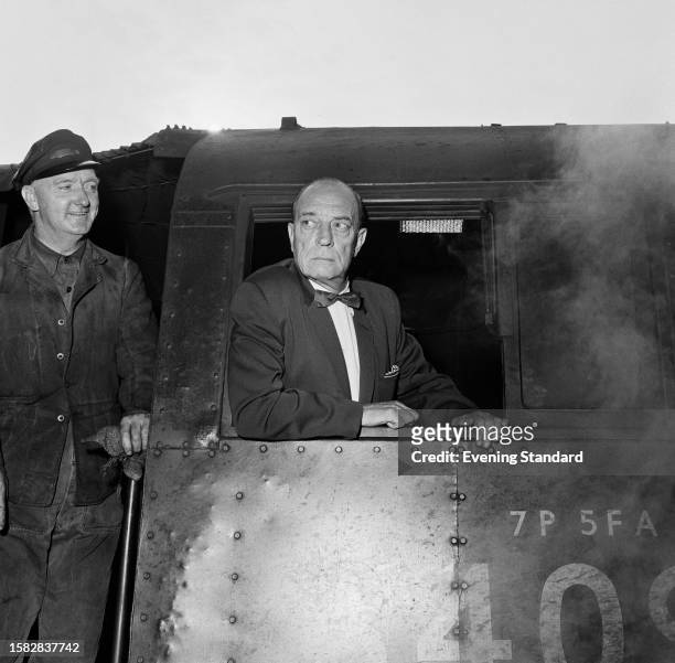 Comic actor Buster Keaton at the window of a locomotive train while driver Alfred Hurley looks on, Waterloo Station, August 12th 1959.