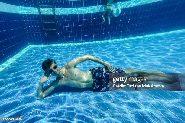 a young man in swimming goggles lies at the bottom of a pool in blue water. - lowest stockfoto's en -beelden