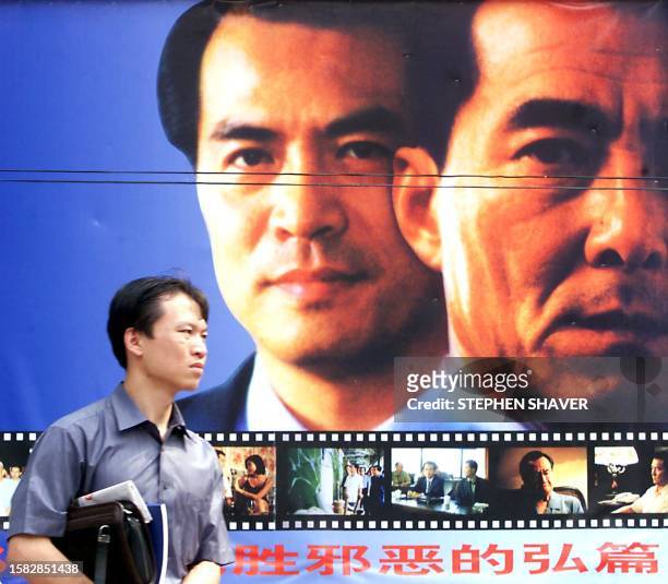 Chinese businessman walks past a large movie poster in Beijing 15 September 2000 advertising a newly released Chinese film about corruption and the...