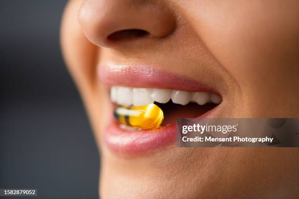 unrecognizable multiracial woman holding pill omega-3 fish oil in mouth between teeth, close-up - menschlicher mund stock-fotos und bilder