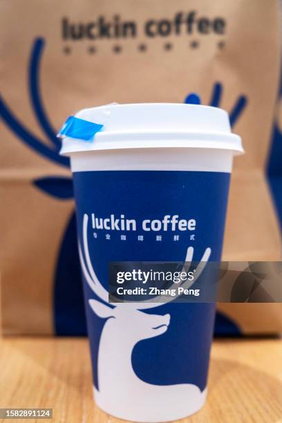 Coffee cup and paper bag printed with iconic deer head silhouette are placed on the table. Luckin Coffee has reported its revenue of 6.2 billion yuan...