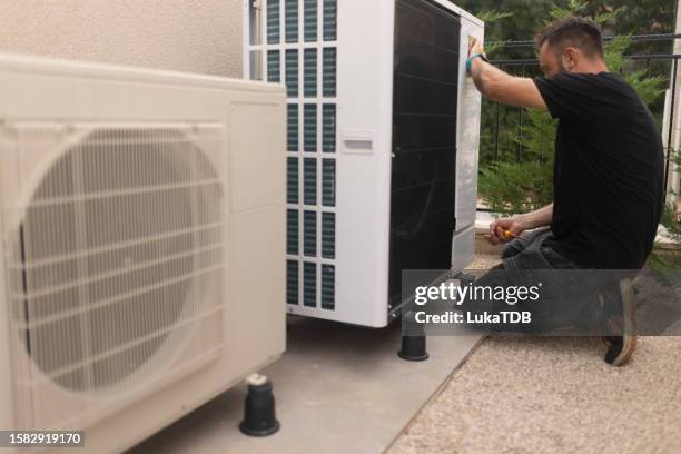 a male electrician is standing in the yard installing a heat pump - replacement stockfoto's en -beelden