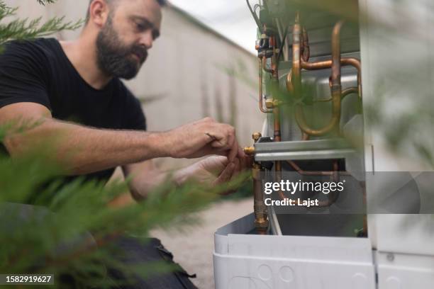 concentrated man installe une pompe à chaleur, extrêmement respectueuse de l’environnement - remplacement photos et images de collection