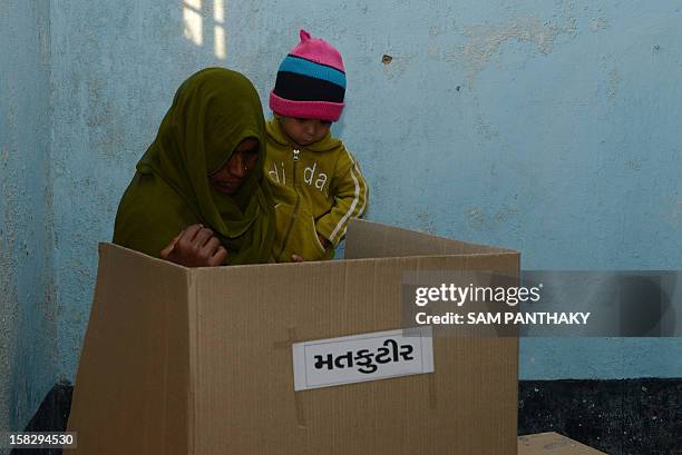 An Indian woman holdS an infant as she casts her vote in the state assembly elections at Sanand, some 30 kms from Ahmedabad on December 13, 2012. The...