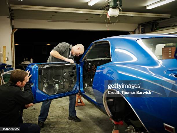 two friends in garage installing door on car - voiture de collection photos et images de collection