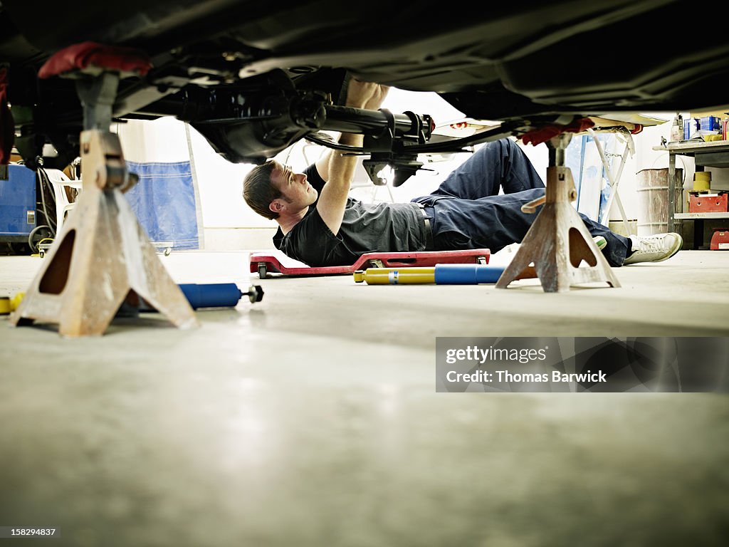 Mechanic lying on floor in garage working on car