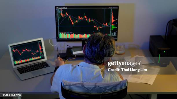 eine rückansicht eines traurigen asiatischen mannes, der mit einem ausdruck von depression oder sorge über die börsenkrise auf seinen laptop schaut, während er in seinem homeoffice sitzt - distressed stock market people stock-fotos und bilder