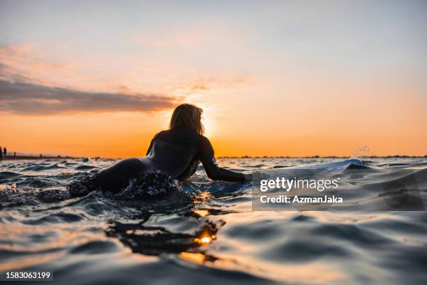 adventurous female surfer jumping on her surfboard in the middle of the ocean and waiting for a wave - surfer stock pictures, royalty-free photos & images
