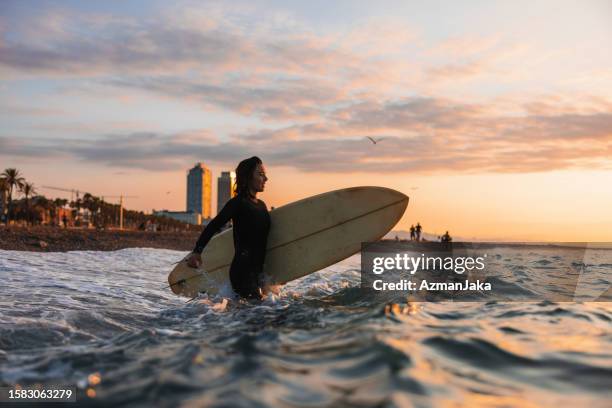 surfeuse professionnelle se précipitant dans l’eau pour pratiquer ses compétences de surf au lever du soleil - province-de-barcelone photos et images de collection