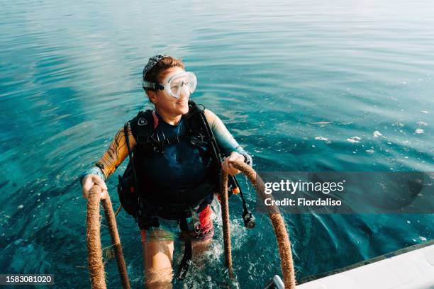 red-haired woman in diving clothes climbing the ladder from the water to the boat - aquatic sport stock pictures, royalty-free photos & images