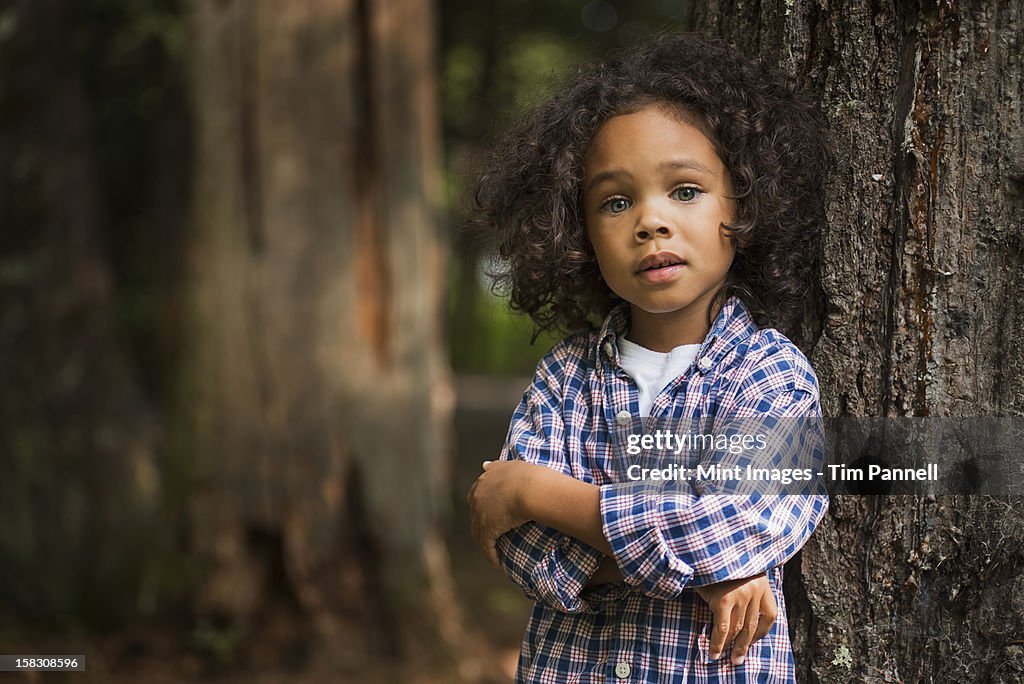 A young boy with arms folded leaning against a tree.