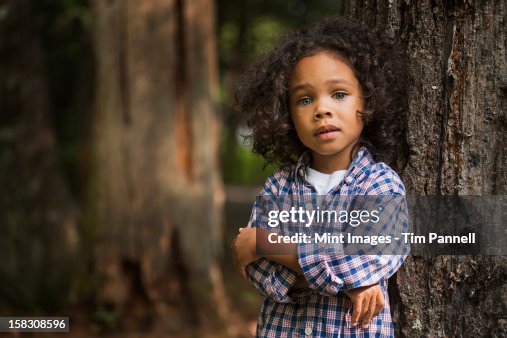 A young boy with arms folded leaning against a tree. A young boy with arms folded leaning against a tree.