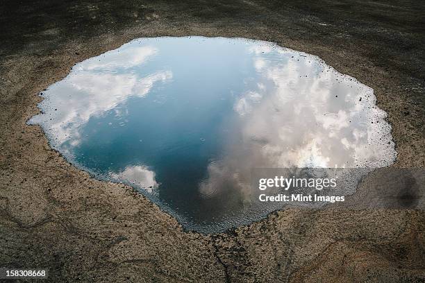 rain drops falling onto a large puddle. a reflection of sky and clouds. - puddle fotografías e imágenes de stock