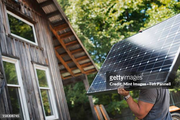 A man carrying a solar panel on a green construction site, working on a green building project.