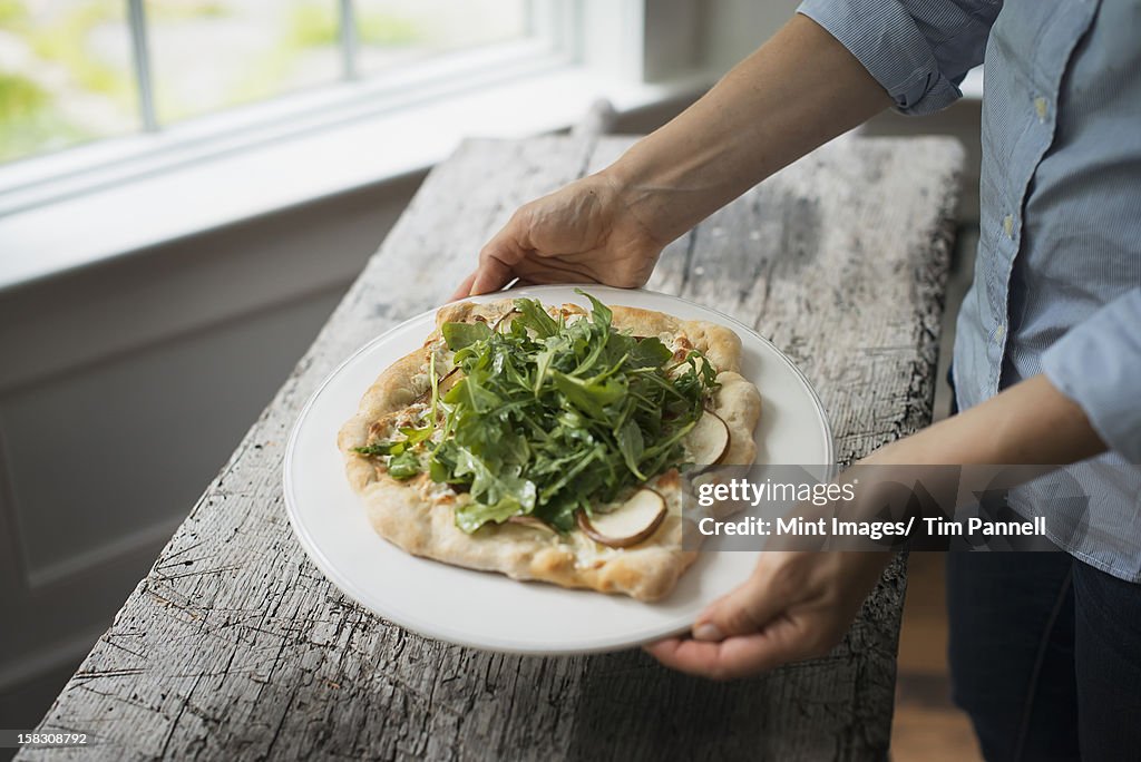 A person holding a plate with fresh salad and ingredients on baked bread.