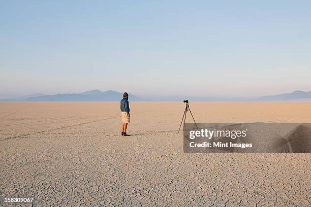 man with camera and tripod on the flat saltpan or playa of black rock desert, nevada. - black rock desert stock pictures, royalty-free photos & images