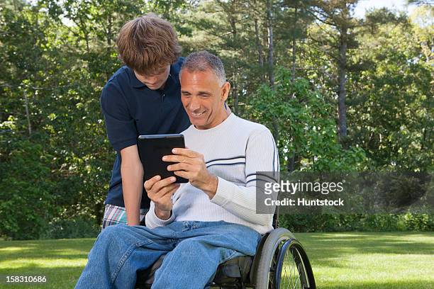 man with spinal cord injury in wheelchair with teen son reading a tablet - duxbury, massachusetts stock pictures, royalty-free photos & images